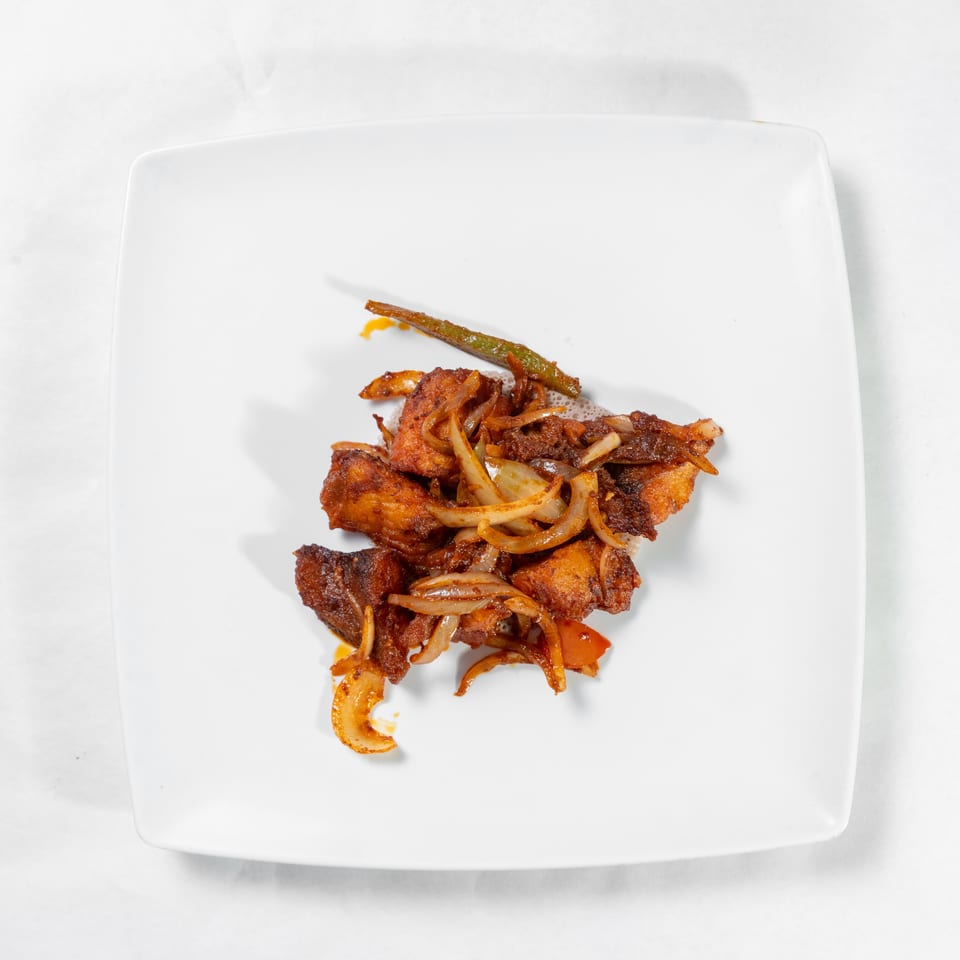 Crispy fried pieces topped with sautéed onions, carrots, and green beans on a white square plate.