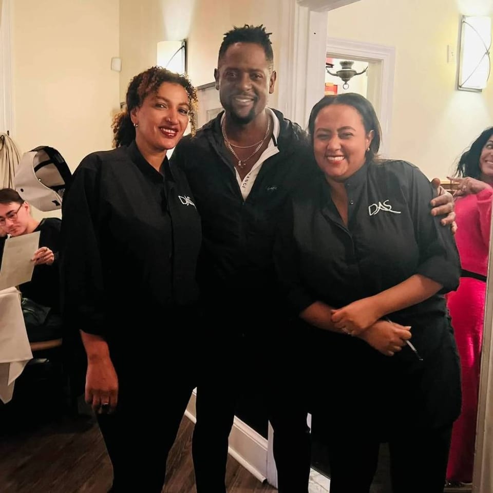 Three smiling restaurant staff members pose together indoors, wearing black shirts with matching logos.