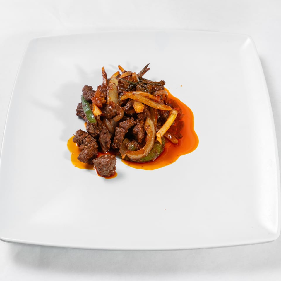 Sliced beef sautéed with onions and green peppers in red chili oil, served on a white square plate.