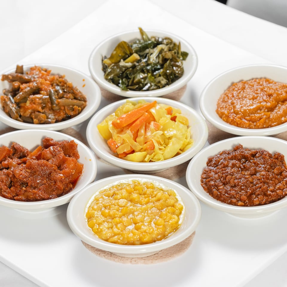 Assortment of colorful stewed vegetables, beans, and legumes served in white bowls on a platter.