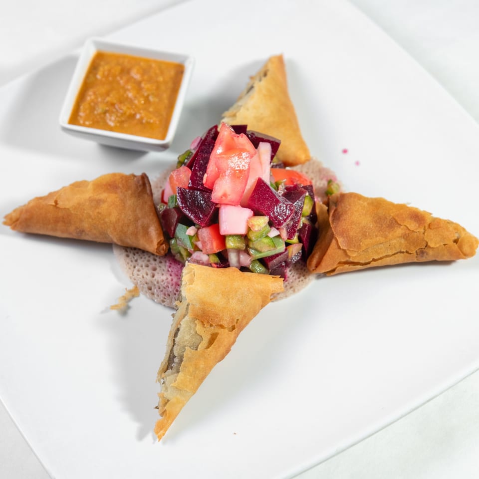 Vegetarian sambusas served with salad and sauce over injera.