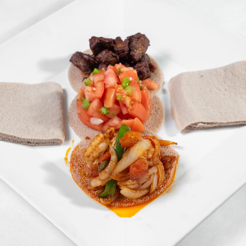Ethiopian platter with injera, spicy shrimp and vegetable stew, diced tomato salad, and grilled meat.